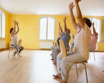 Image of a group of people doing stretching exercises in chairs in a bright room.