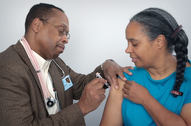 Physician giving a woman a vaccination shot in the arm.