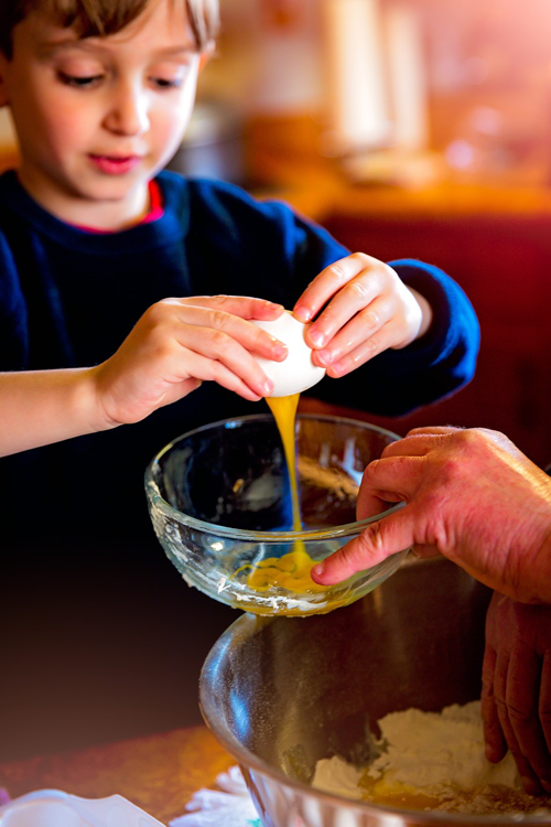 Niño pequeño rompiendo un huevo en un tazón de ingredientes para hornear