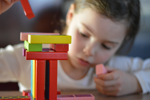 A young girl building a tower out of colorful wooden blocks